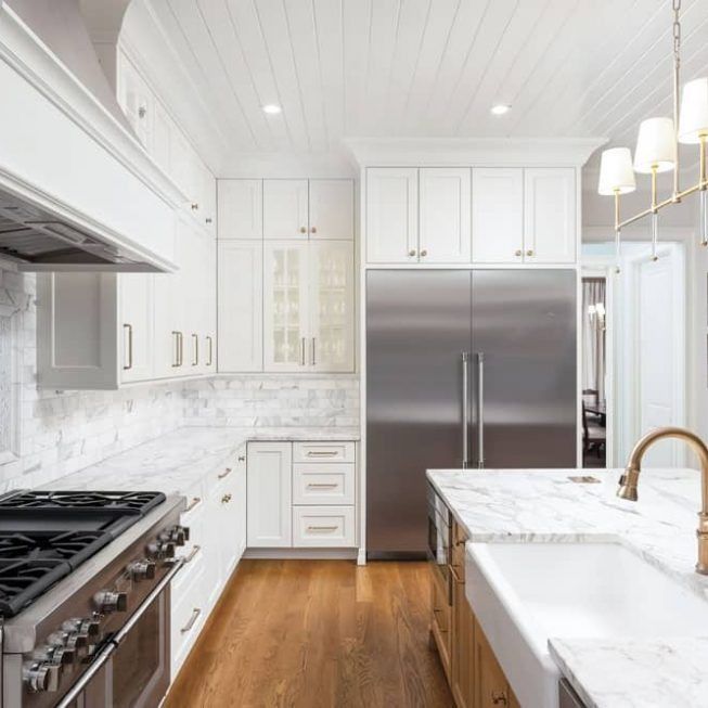 Bright white kitchen with marble counters, stainless steel appliances, and warm wood flooring
