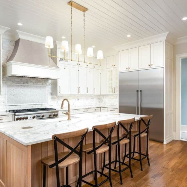 Bright white modern kitchen with marble island, bar stools, and stainless steel refrigerator