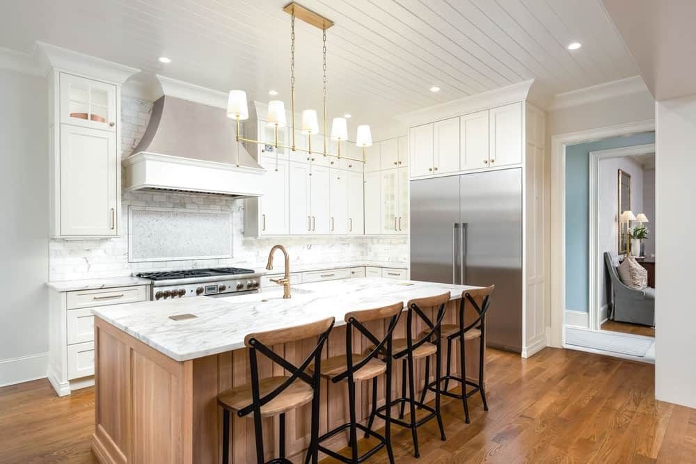 Bright white kitchen with a marble island, three barstools, and stainless steel appliances