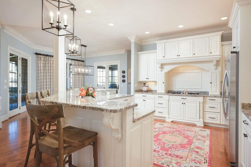 Bright kitchen with white cabinets, marble island, pendant lights, and pink patterned rug