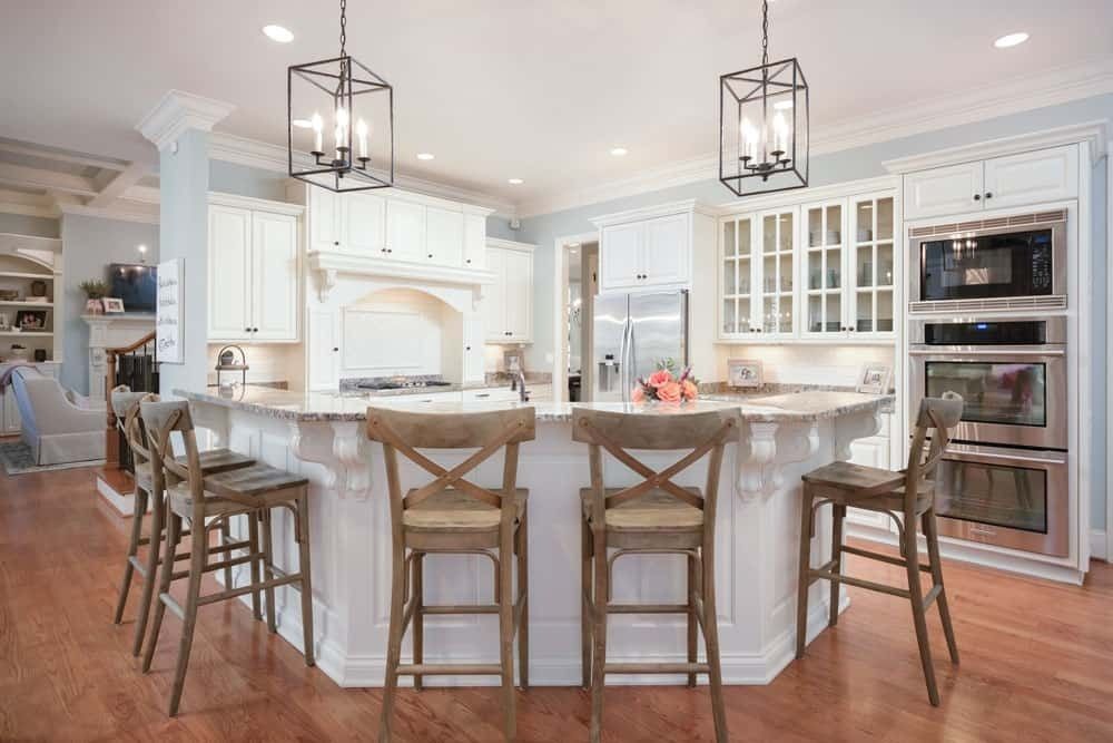 Bright white kitchen with a large island, bar stools, pendant lights, and wood floors