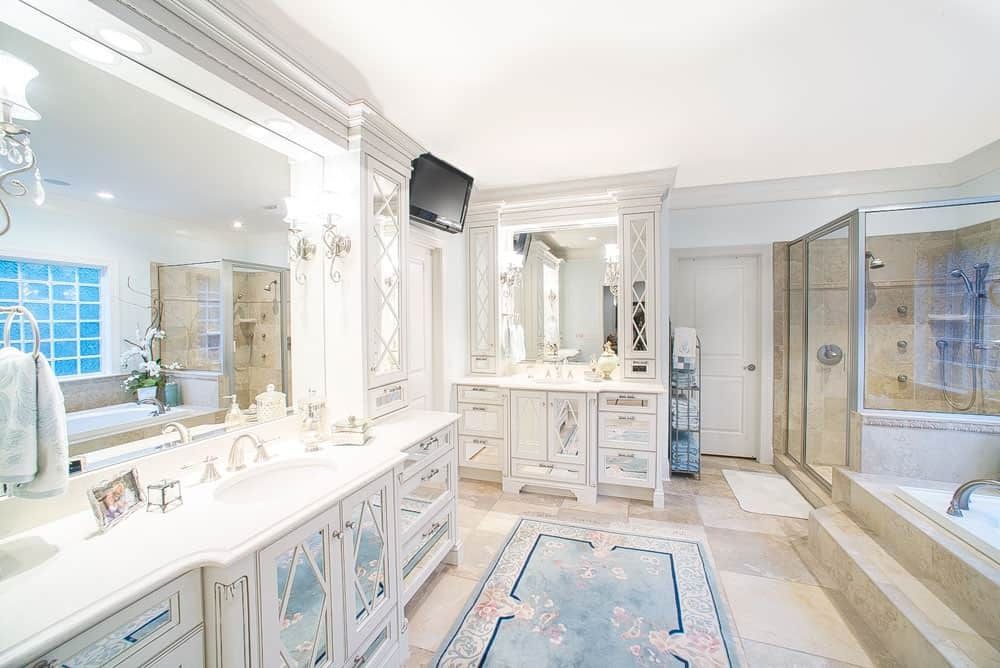 Bright luxury bathroom with double vanity, large mirror, glass shower, tub, and blue accents