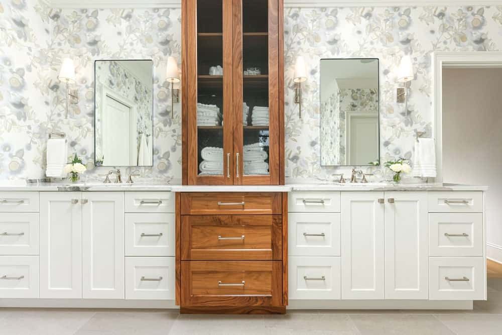 White bathroom vanity with double mirrors, marble counters, and a central wooden cabinet wall panel.