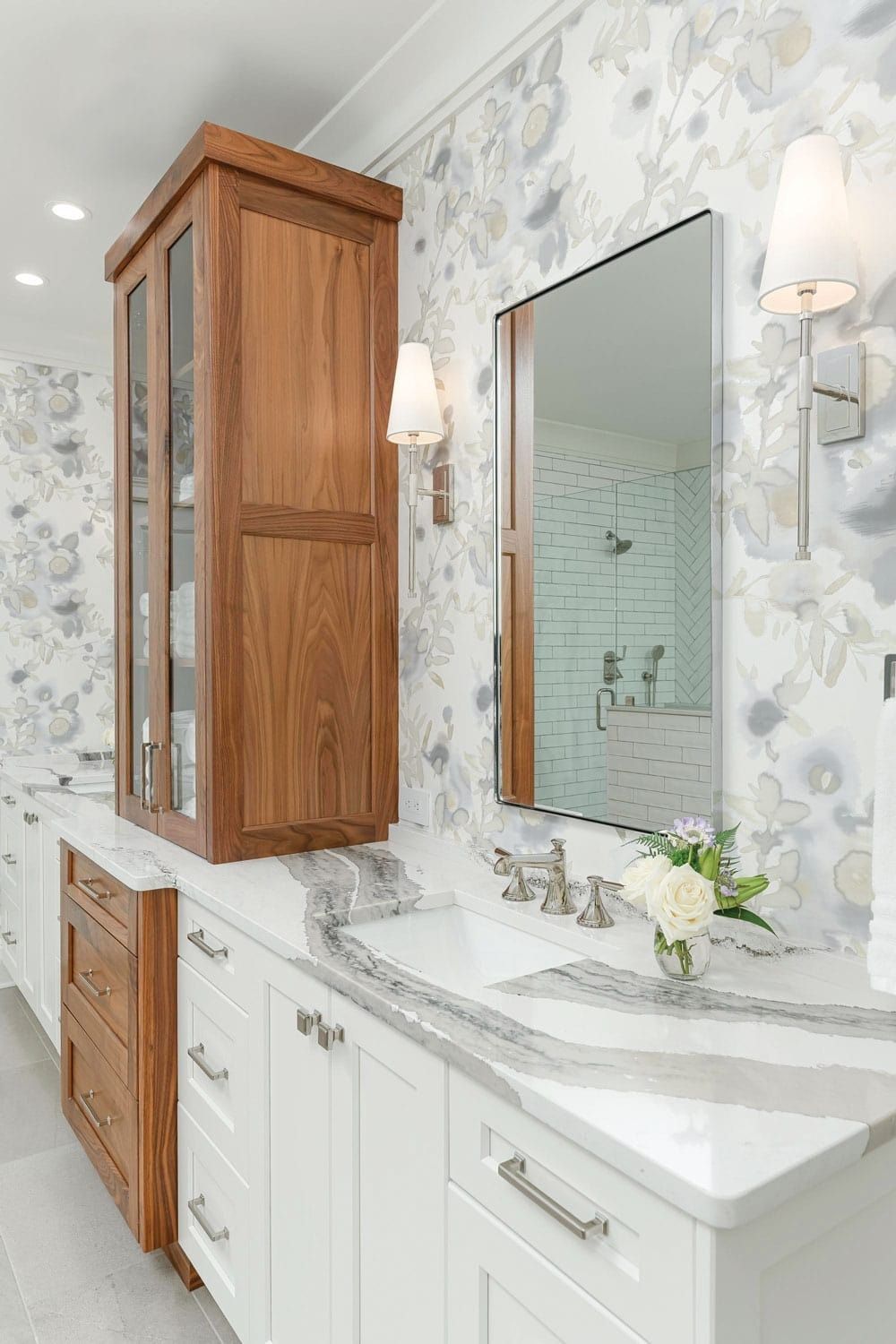 Bathroom vanity with wood cabinets, white countertop, mirror, and floral wallpaper.