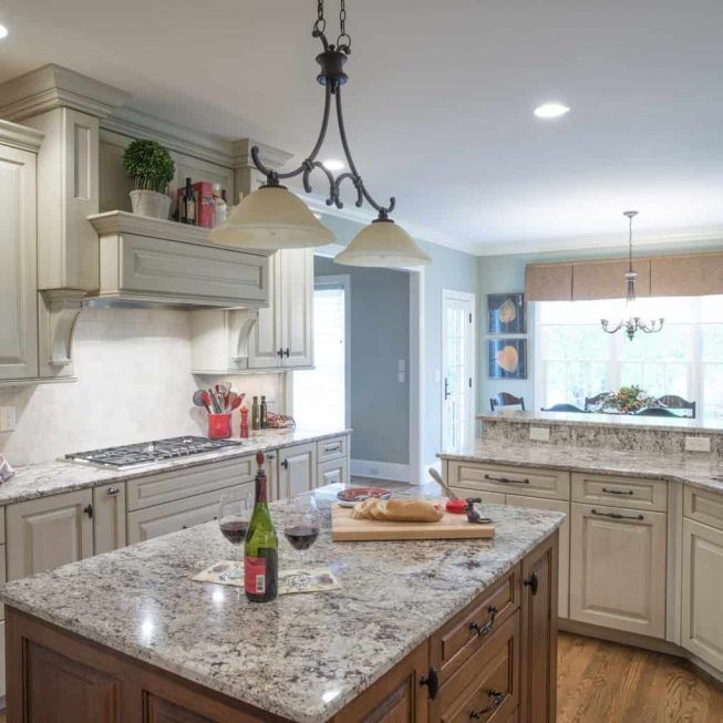 Bright, modern kitchen with granite island, cream cabinets, and pendant lights by a windowed breakfast nook