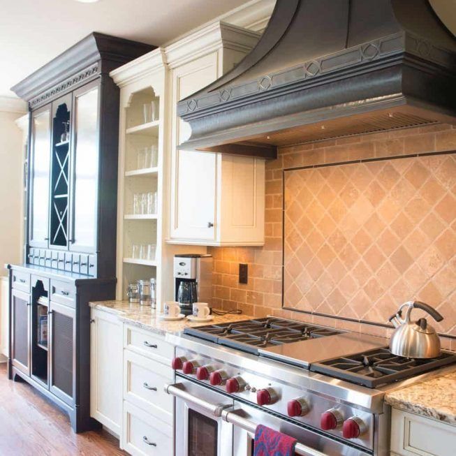 Elegant cream kitchen with stainless steel stove, dark range hood, and beige tile backsplash