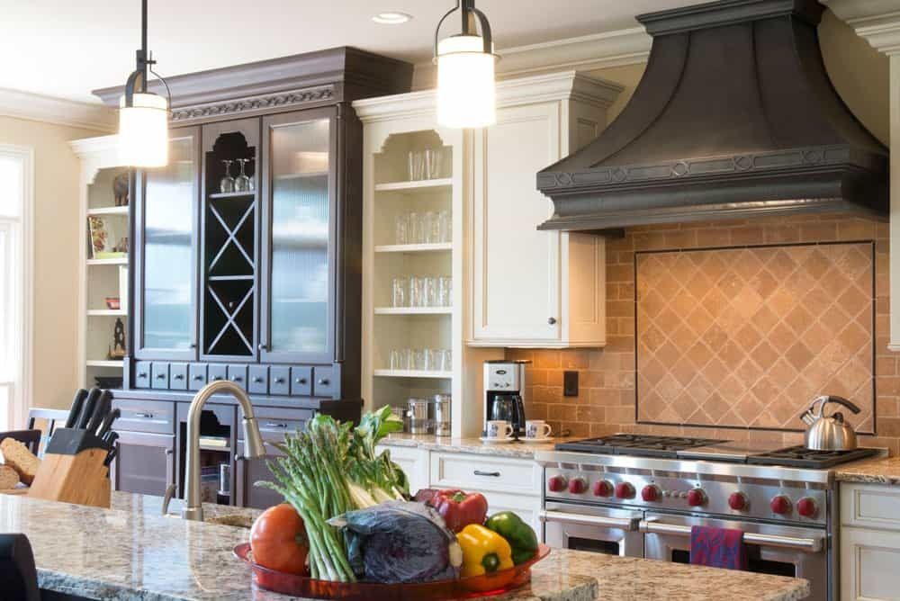 Modern kitchen with dark wood cabinets, granite island, pendant lights, stainless range, and fruit bowl