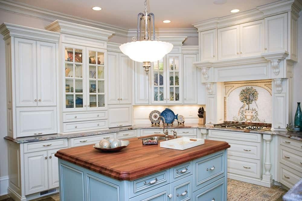 Elegant white kitchen with blue island, wood countertop, and chandelier lighting