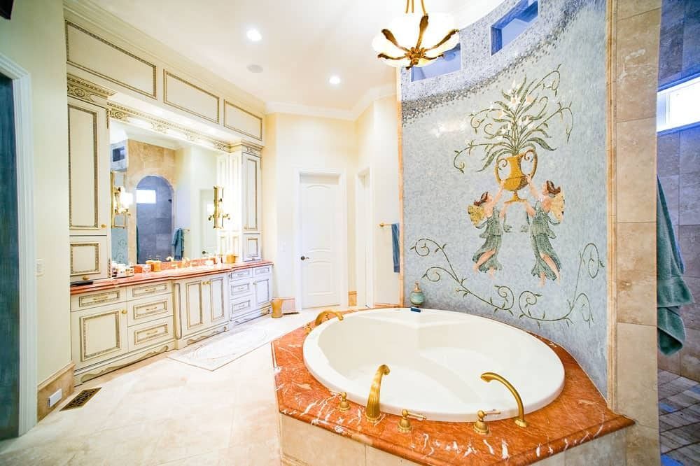 Bright bathroom with ornate vanity, tiled walls, and a large round soaking tub on a red marble platform