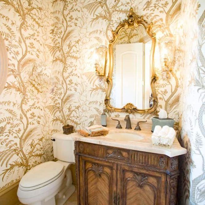 Elegant bathroom with gold wallpaper, ornate mirror, and white sink vanity beside a toilet
