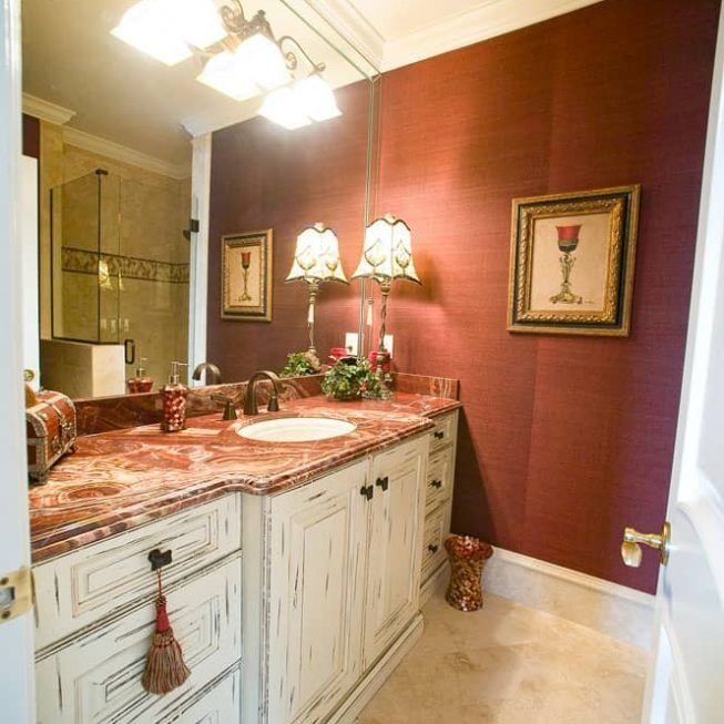 Elegant bathroom vanity with marble countertop, red walls, ornate mirror, and twin table lamps