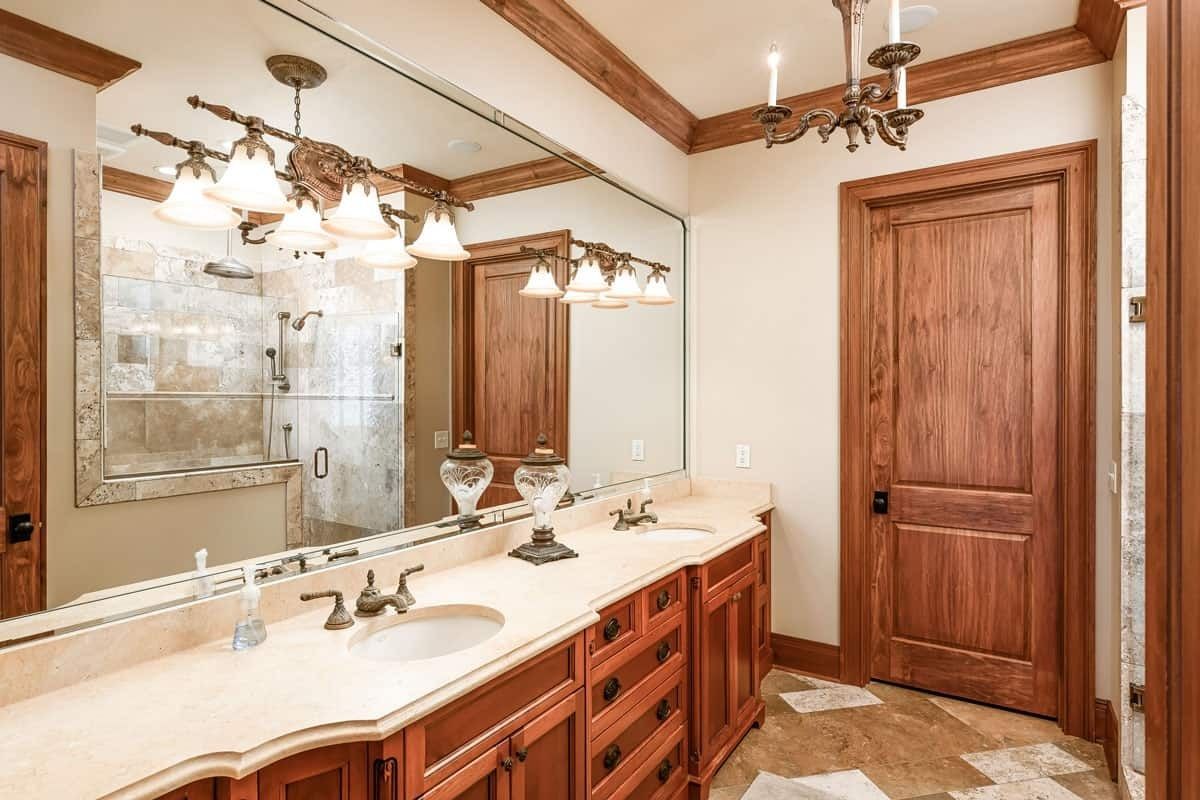 Elegant bathroom with double vanity, large mirror, glass shower, wood cabinets, and coffered ceiling