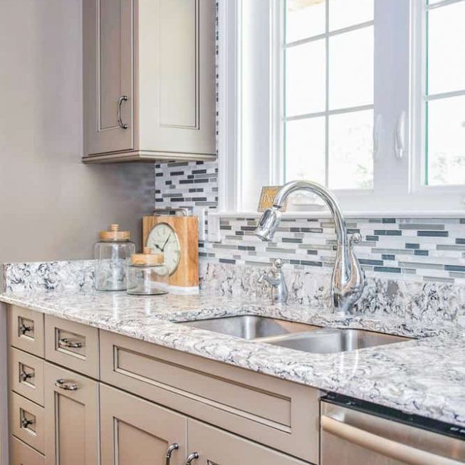 Modern kitchen countertop with sink, chrome faucet, beige cabinets, and mosaic tile backsplash by a window