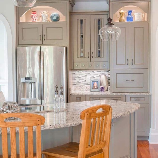 Bright kitchen with gray cabinets, granite island, stainless fridge, and two wooden stools.