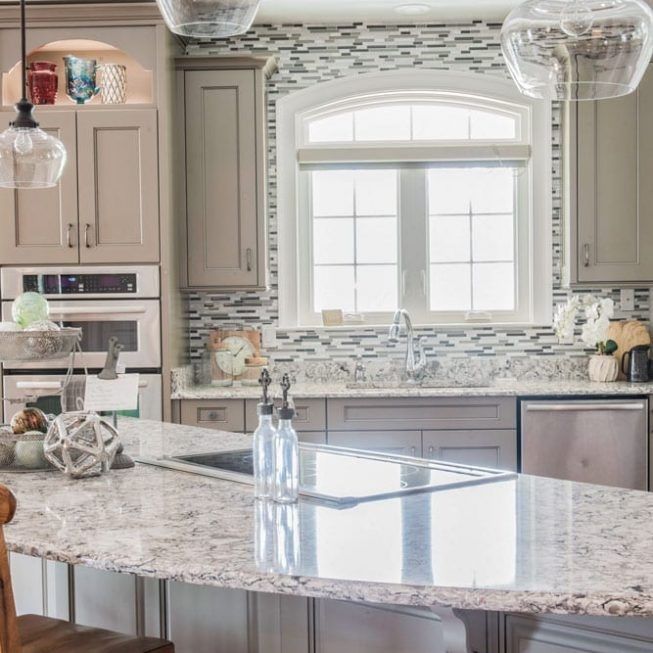 Bright modern kitchen with marble island, gray cabinets, mosaic backsplash, and large window