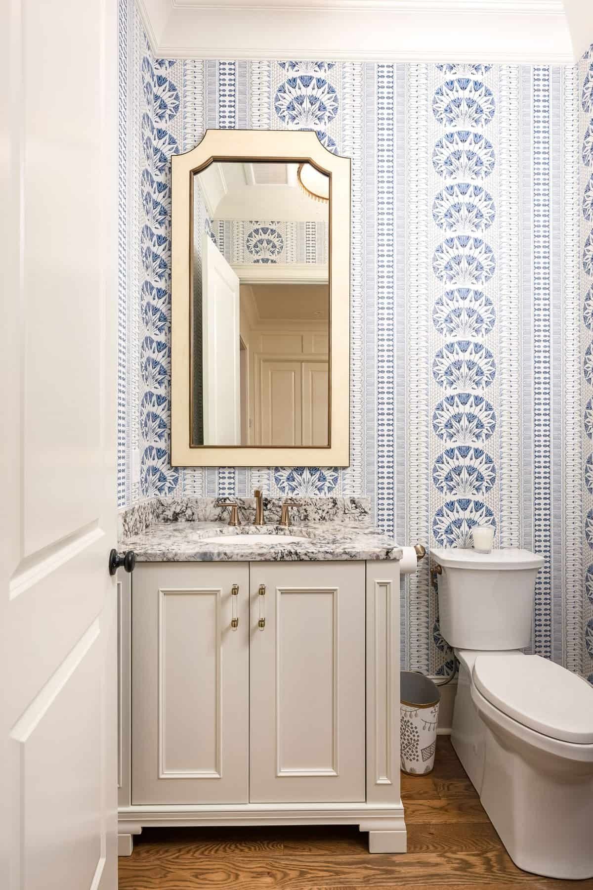 Small bathroom with blue patterned wallpaper, white vanity, mirror, and toilet.