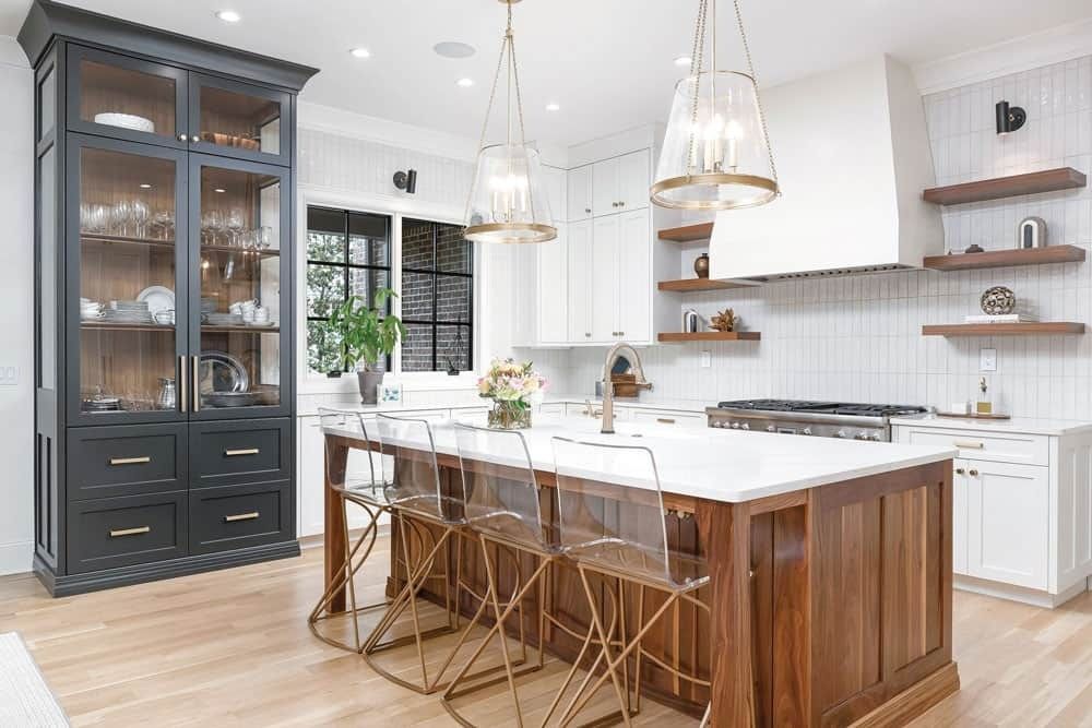 Bright modern kitchen with white cabinets, wood island, pendant lights, and dark glass display cabinet
