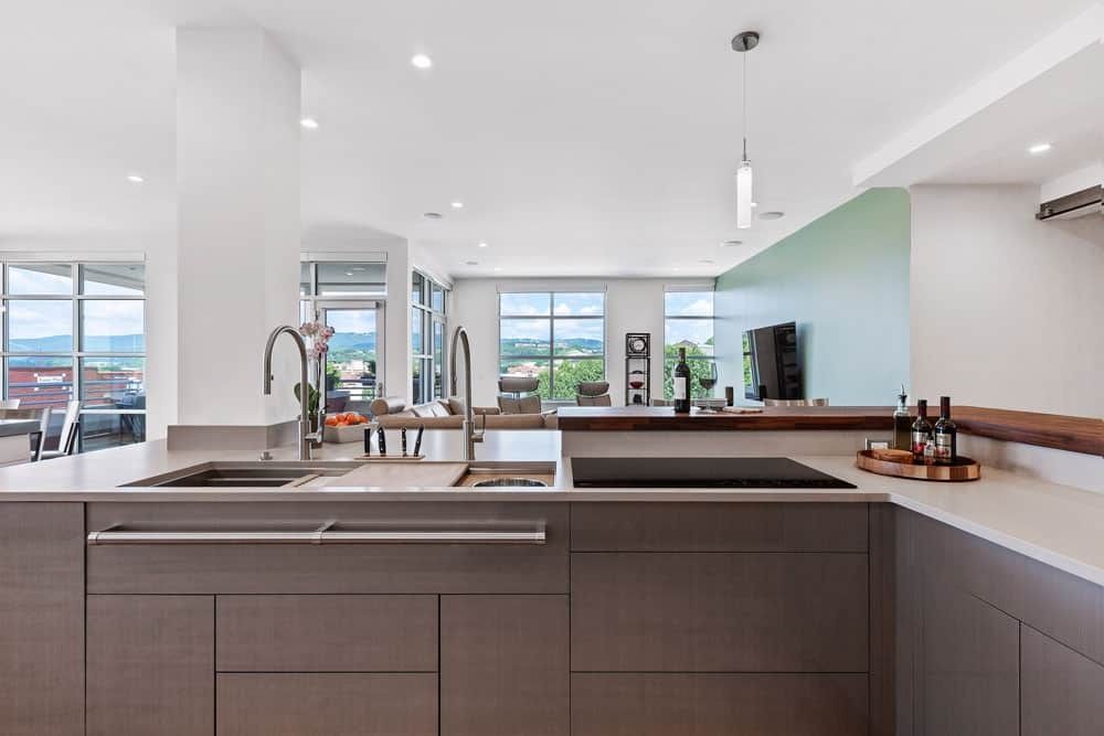 Modern open-plan kitchen with a large island, white ceilings, and bright windows overlooking a scenic view