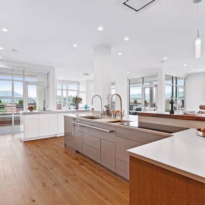 Bright modern kitchen with white cabinets, wood floors, large windows, and a central island with sink