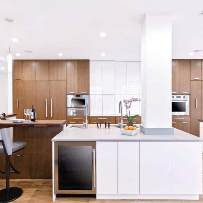 Modern white kitchen with wood cabinets, island, built-in appliances, and a vase of flowers