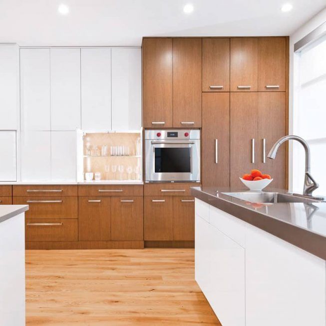 Bright modern kitchen with white cabinets, wood flooring, built-in oven, and island sink
