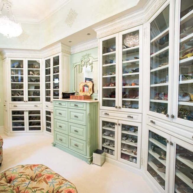 Bright walk-in closet with white glass-front cabinets and a mint green dresser