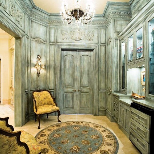 Elegant vintage entry hall with blue-gray paneled walls, chandelier, ornate chair, and round rug