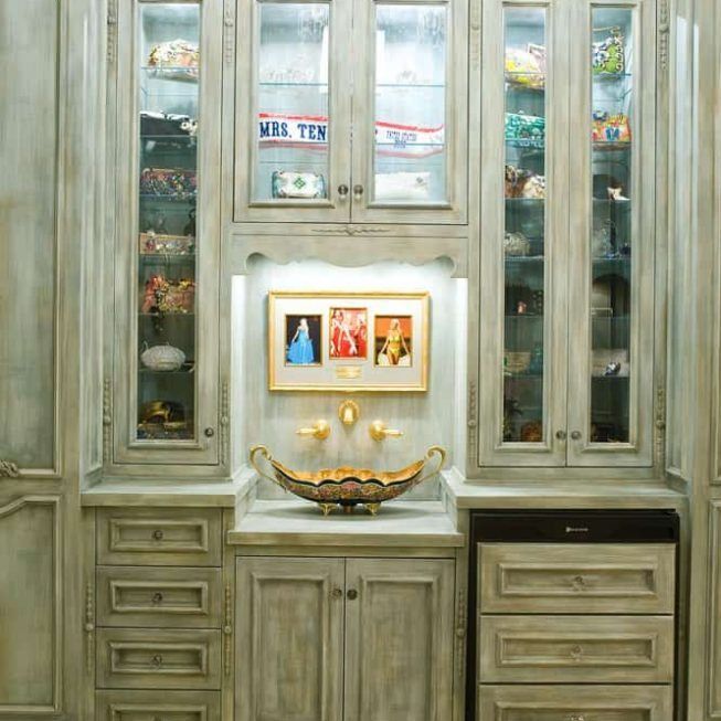 Elegant bathroom vanity with glass-front cabinets, gold sink, and framed art in a softly lit alcove