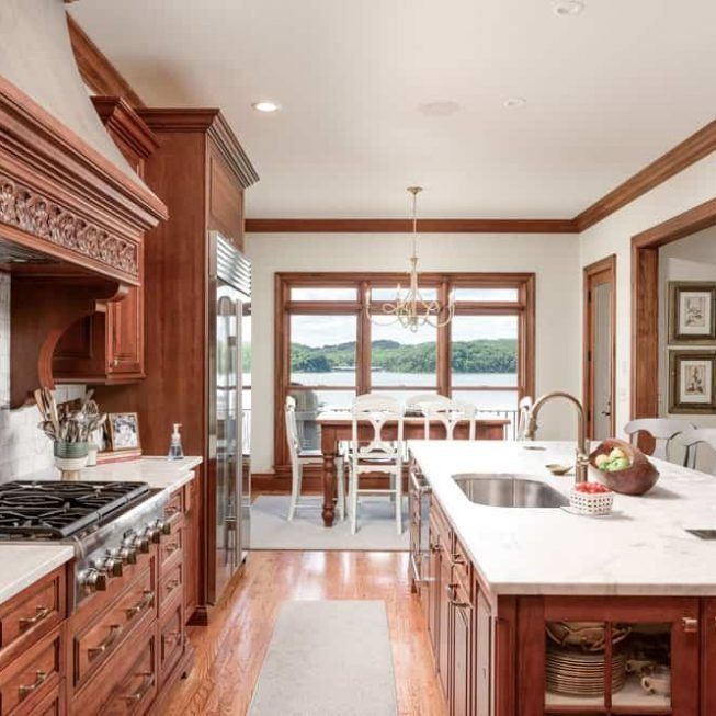 Bright kitchen with wood cabinets, marble island, and lake view through large windows