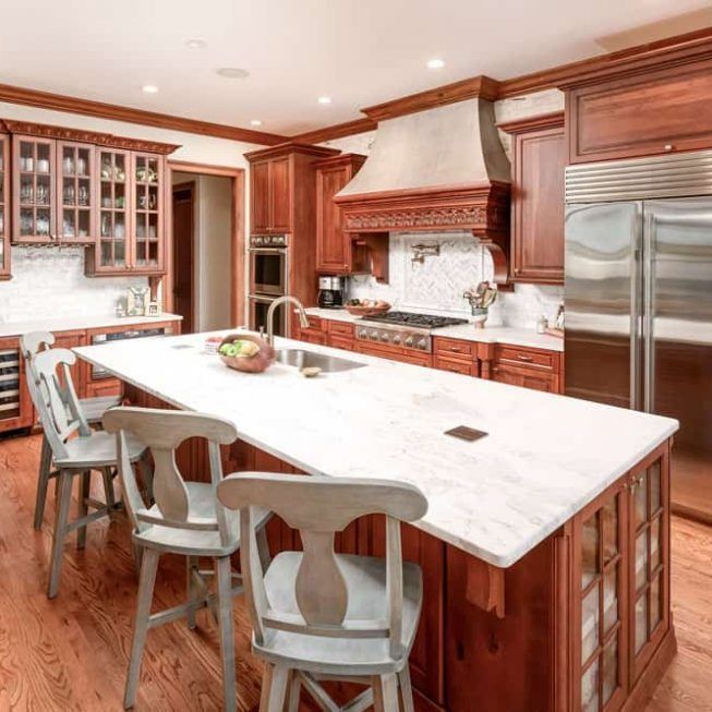 Modern kitchen with cherry wood cabinets, marble island, stainless fridge, and three stools