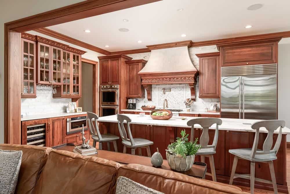 Warm kitchen with wood cabinetry, large island, stainless steel range, and barstools in a bright open layout