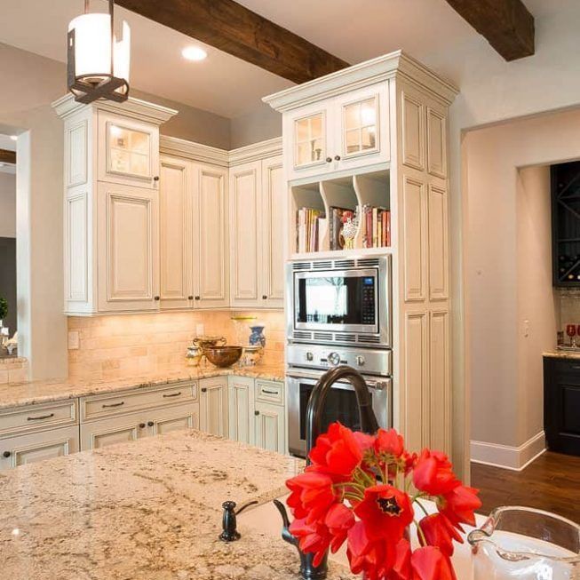 Bright cream kitchen with island, built-in oven, and red flowers in the foreground
