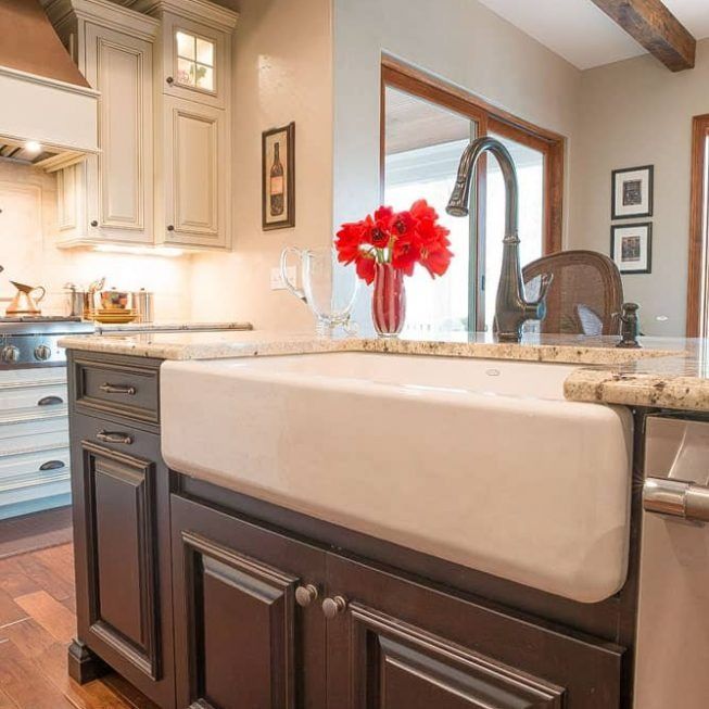 Modern kitchen with farmhouse sink, dark cabinets, beige countertops, and red flowers by the window