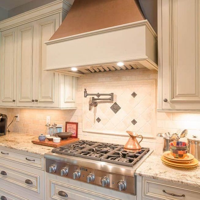 Elegant cream kitchen with stainless steel range, copper hood, and tiled backsplash