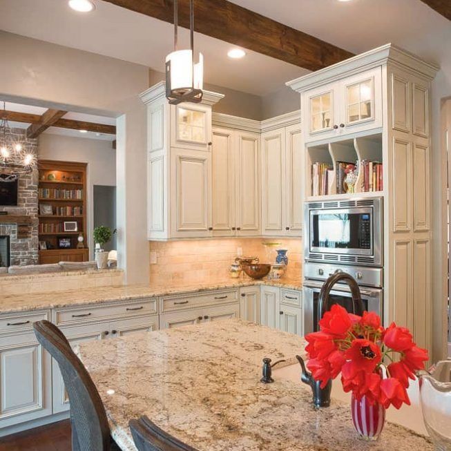 Bright kitchen with cream cabinets, granite island, built-in oven, and red flowers in a vase