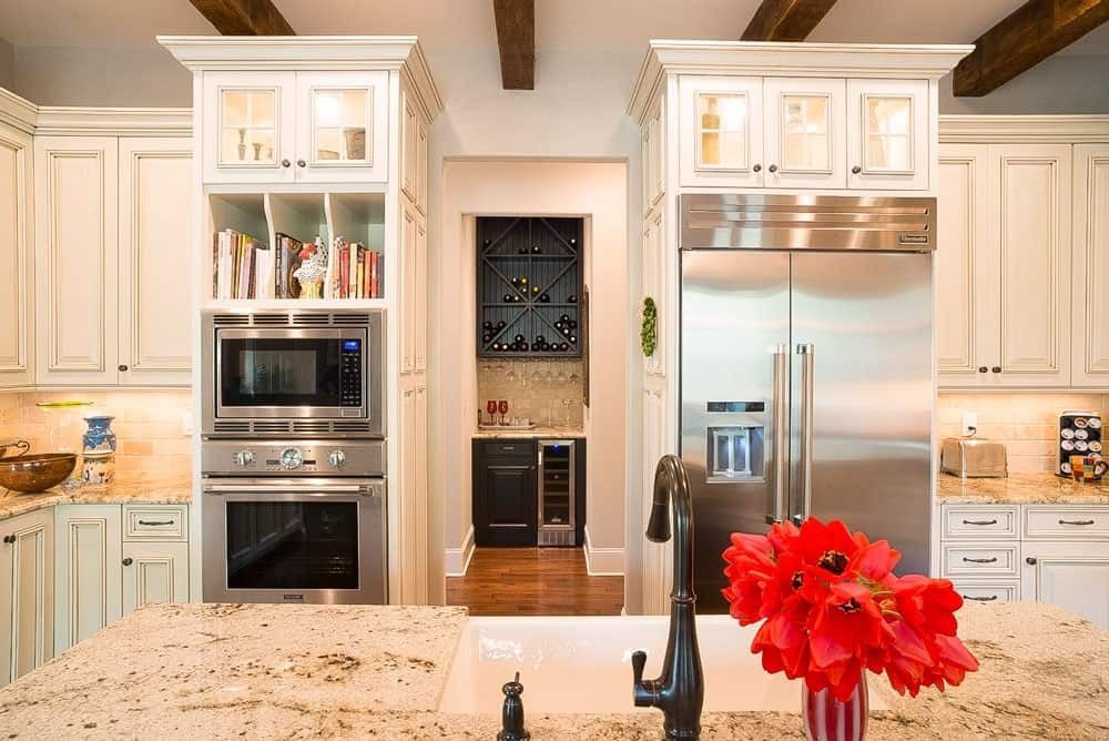 Bright modern kitchen with stainless steel appliances, white cabinets, and red flowers on a granite island