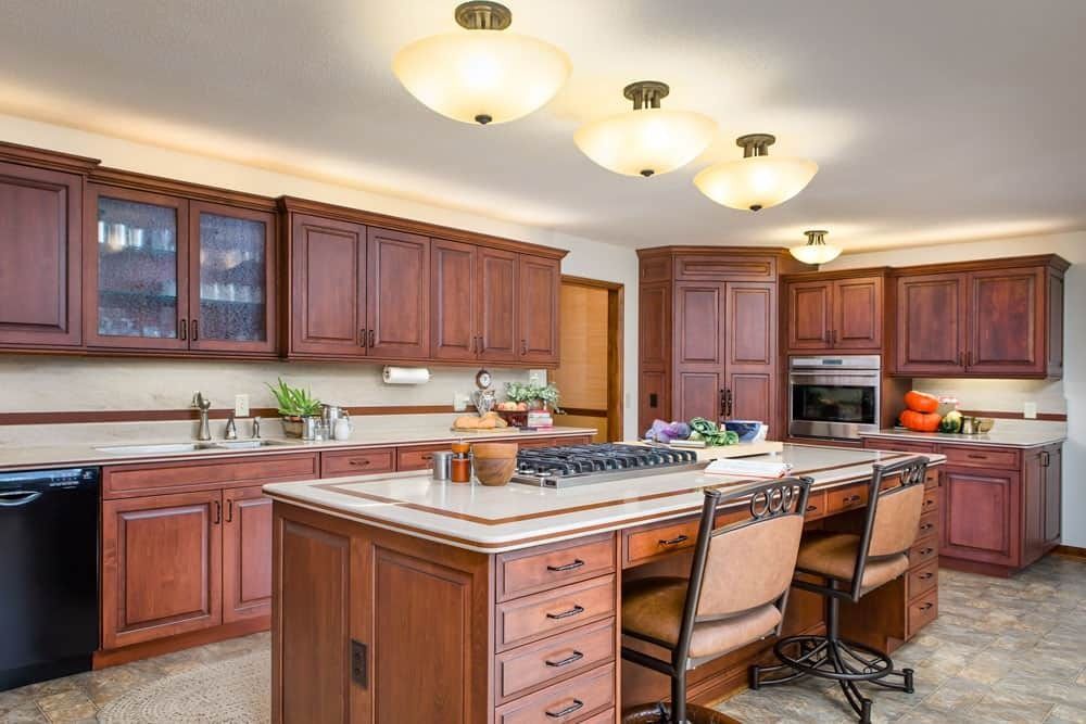 Spacious kitchen with dark wood cabinets, island, and white countertops under warm ceiling lights