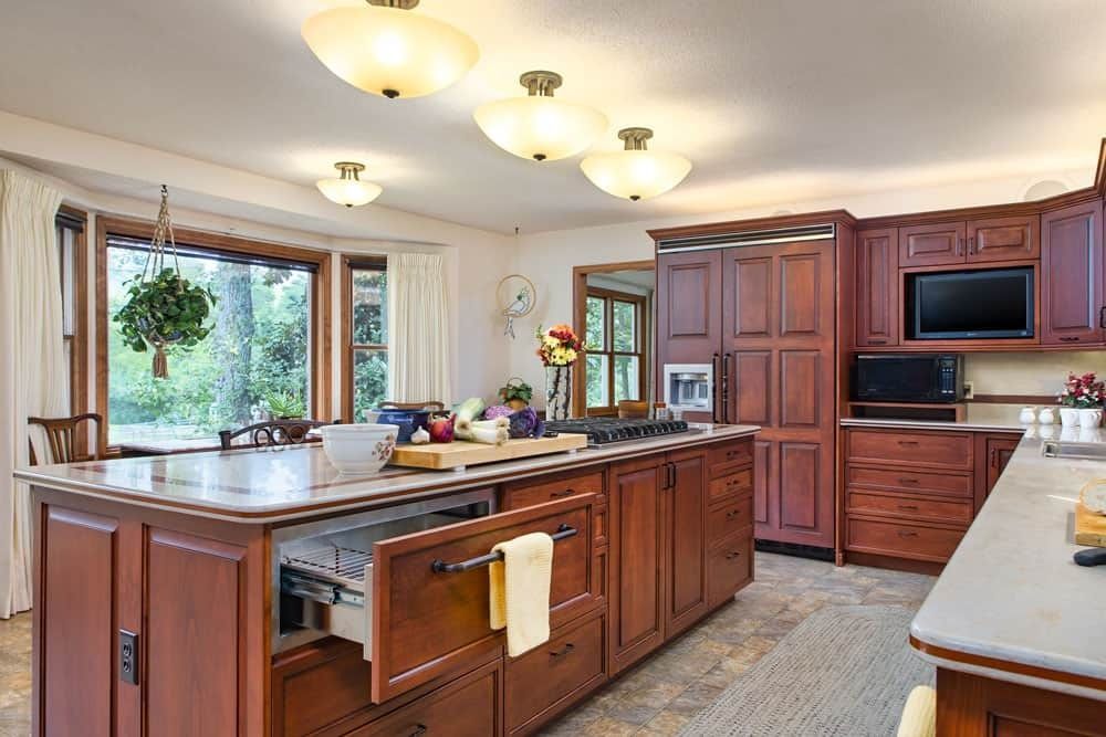 Bright kitchen with wood cabinets, island sink, hanging lights, and a large window over the counter.