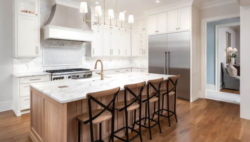 Bright white modern kitchen with island, pendant lights, wood stools, and hardwood floors