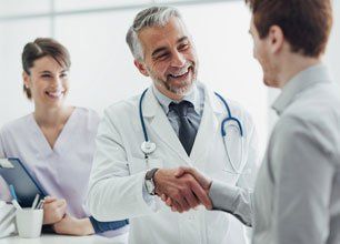 Smiling doctor at the clinic giving a handshake to his patient