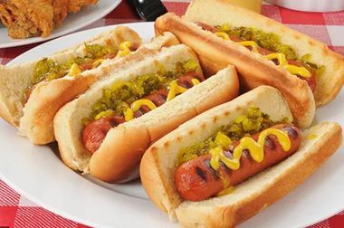 A plate of hot dogs with mustard and pickles on a table.