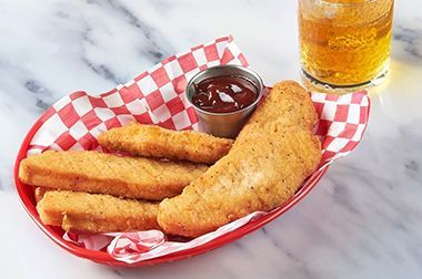 A basket of chicken fingers with ketchup and a glass of beer.