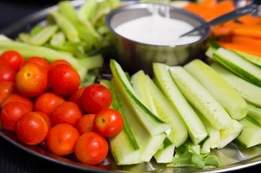 A plate of vegetables including tomatoes , cucumbers , celery and carrots with a dipping sauce.