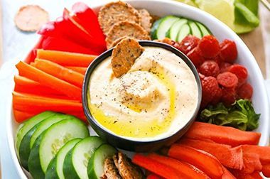 There is a bowl of dip surrounded by vegetables and crackers.