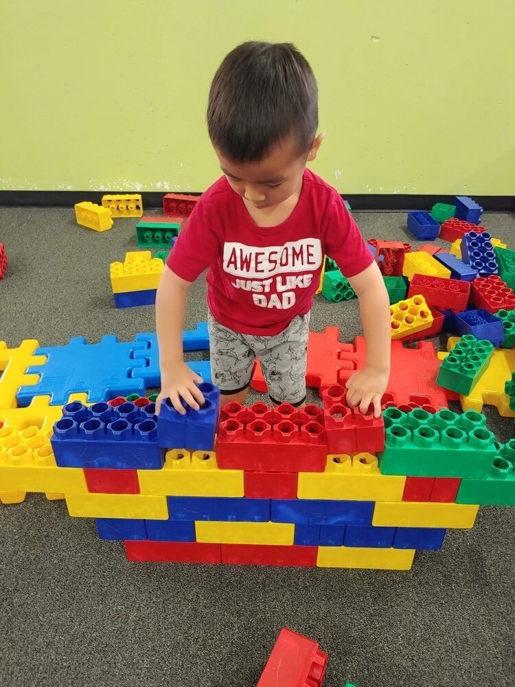 A young boy wearing a red shirt that says awesome just like dad is playing with lego blocks.