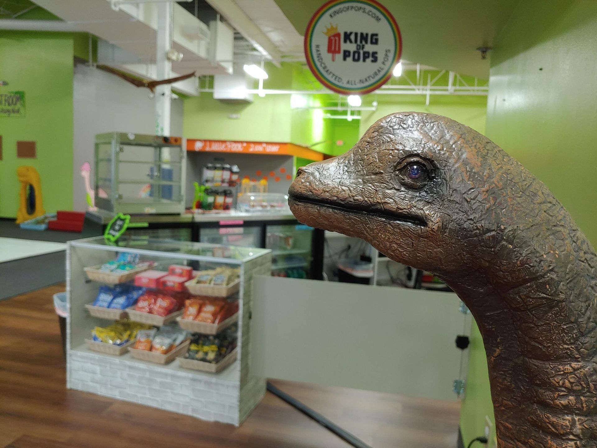 A statue of a dinosaur is standing in front of a store called king pops