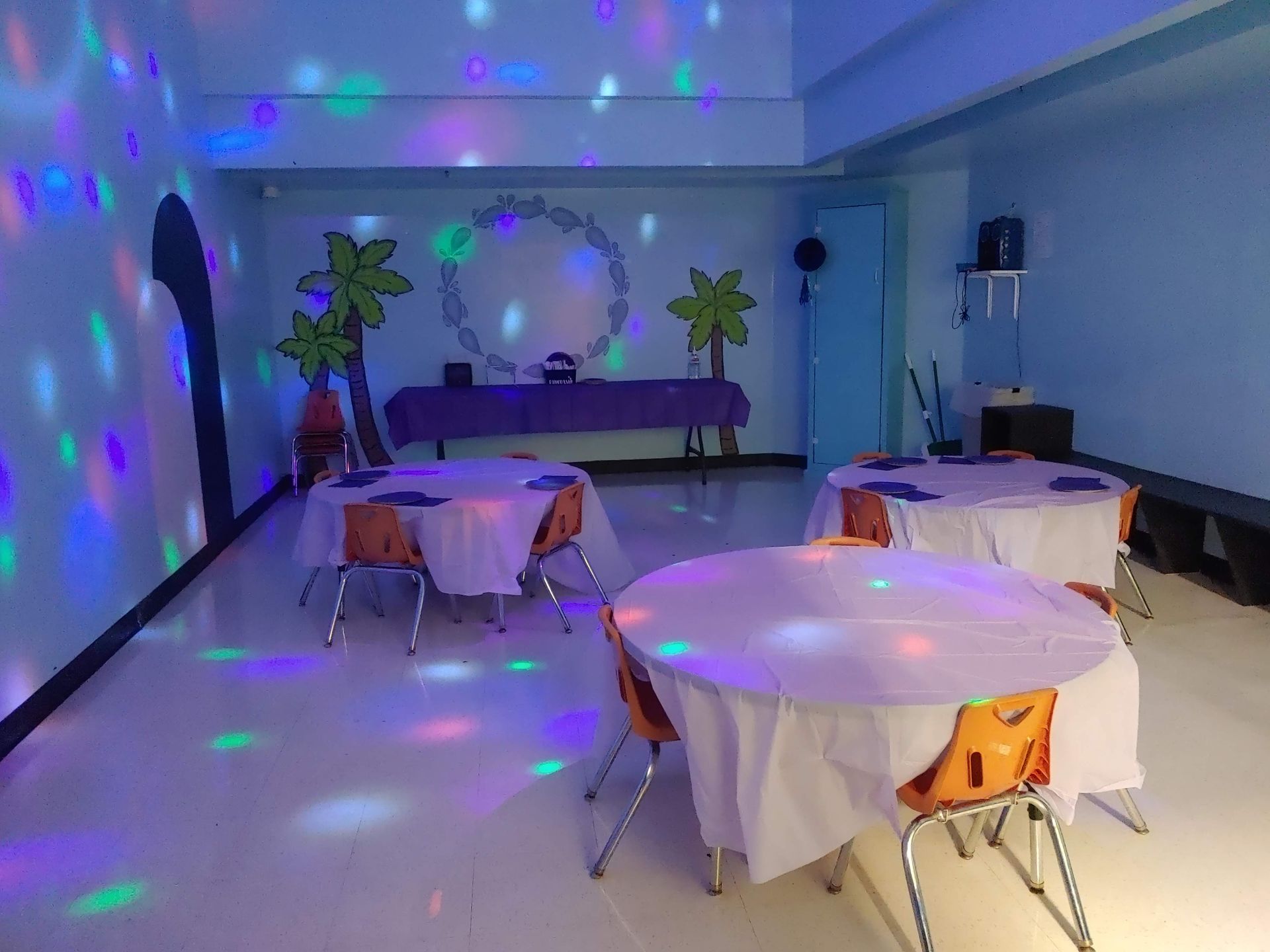 A room with tables and chairs and disco lights on the floor.