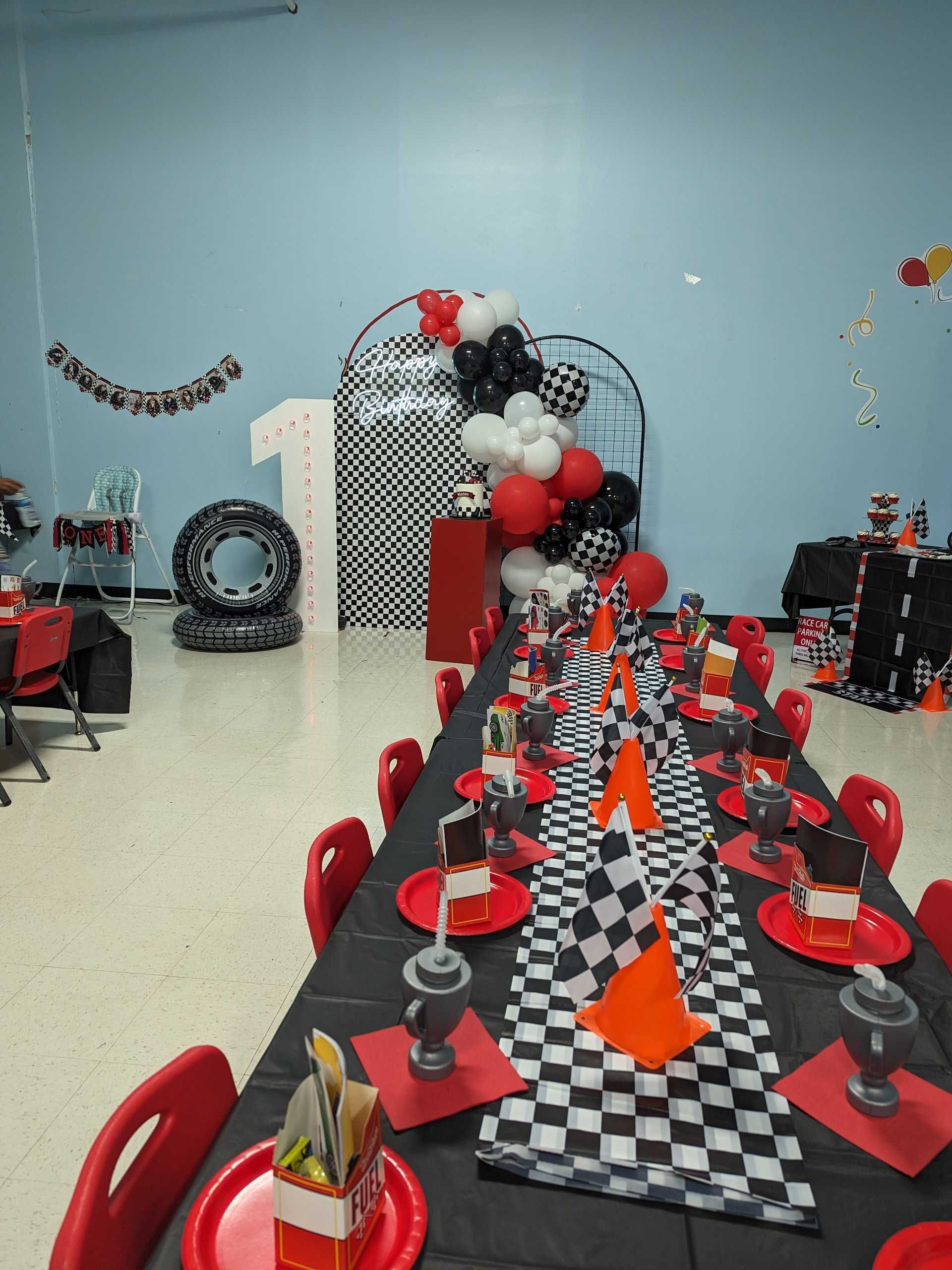 A long table with plates , cups , balloons and a checkered table runner.