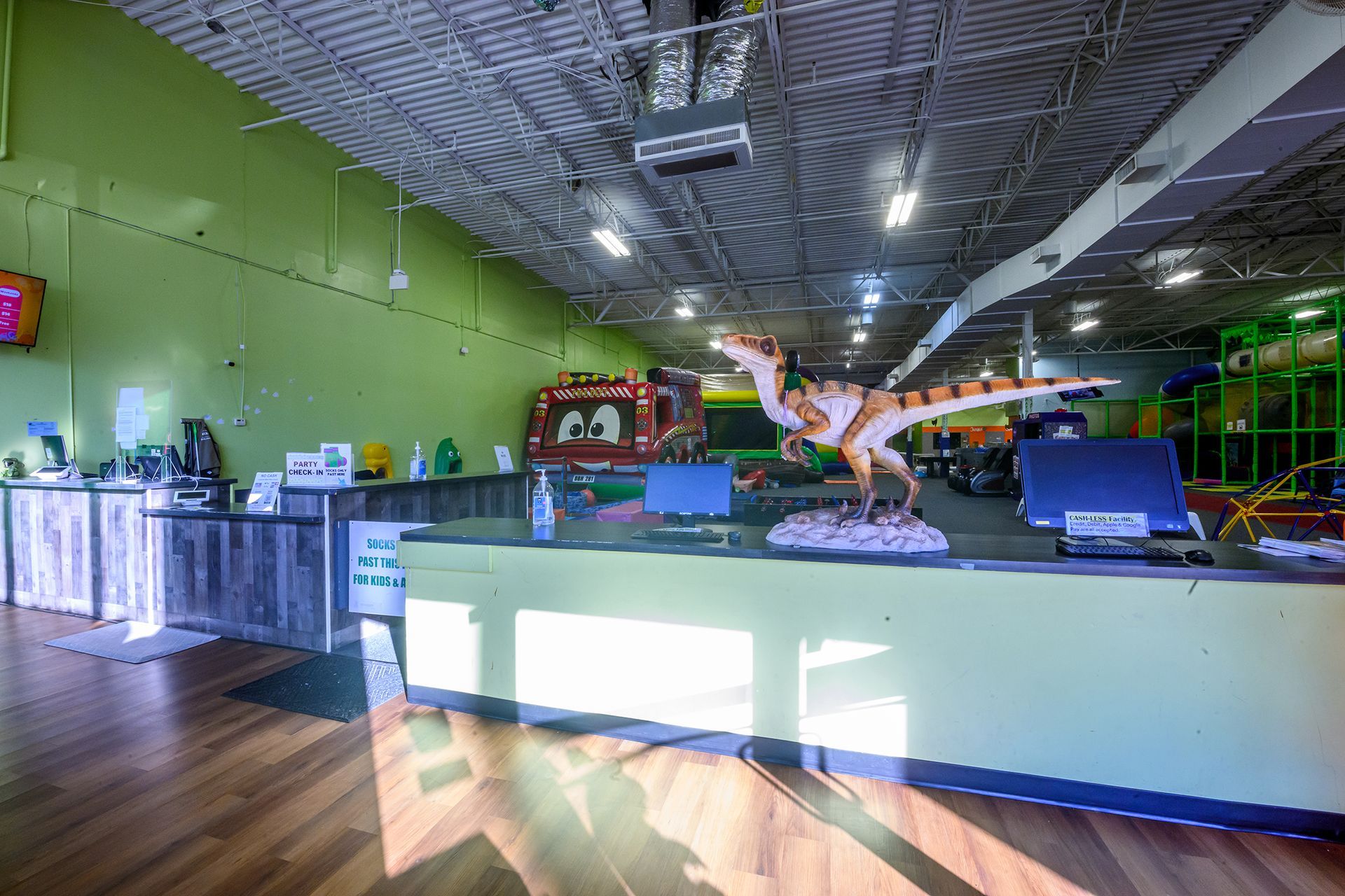 Reception desk in a brightly lit play area, with a dinosaur statue and bounce house visible in the background.