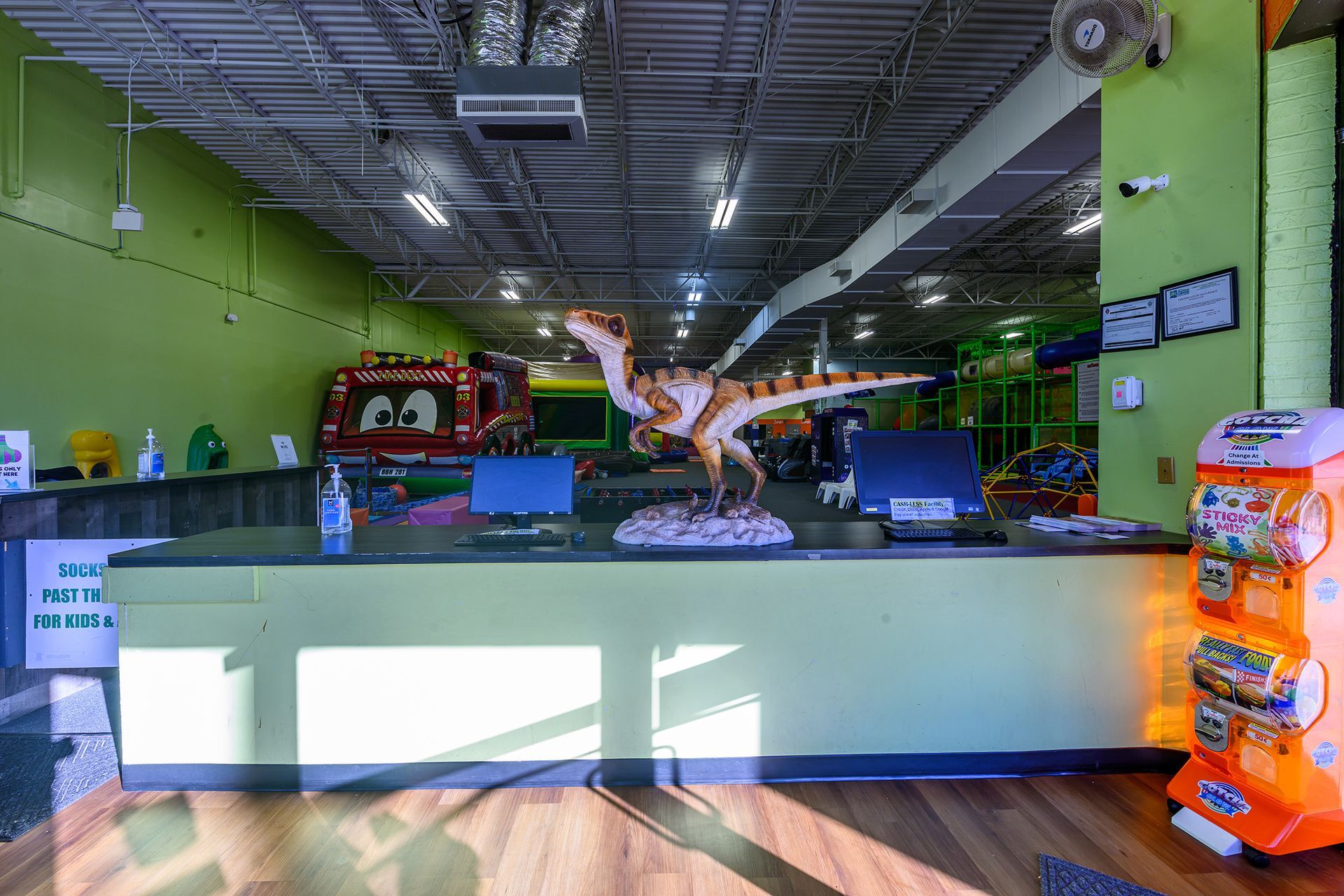 Dinosaur-themed indoor play area: reception desk with dinosaur statue, bounce house in the background.